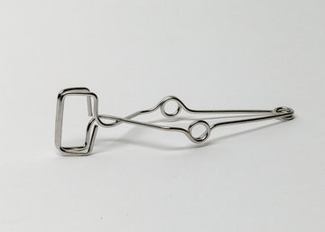 Das Bild zeigt eine metallene Klammer mit einem rechteckigen Greifmechanismus und zwei runden Öffnungen. Diese Klammer könnte für verschiedene Experimente im Bildungsbereich verwendet werden, um Materialien zu fixieren oder zu halten.