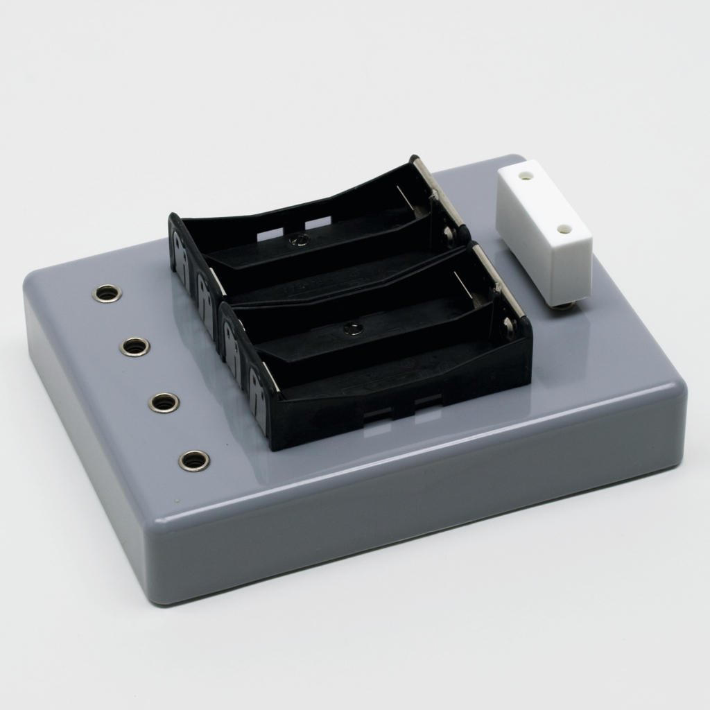 Das Bild zeigt eine graue Experimentierplatte mit zwei schwarzen Batteriehaltern und mehreren Anschlüssen. Sie ist für den Einsatz im Bildungsbereich konzipiert, um elektrische Experimente zu ermöglichen.
