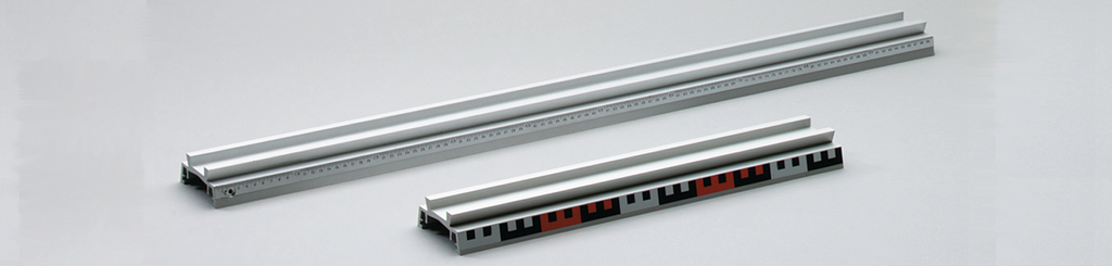 Das Bild zeigt zwei Aluminium-Schienen mit integrierter Skala für präzise Messungen. Die längere Schiene ist für größere Objekte ausgelegt, während die kürzere Schiene zusätzliche Markierungen zur Unterstützung von Experimenten bietet.