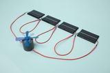 Das Bild zeigt ein Experimentier-Set mit mehreren Solarpanelen, die durch rote Kabel mit einem kleinen elektrischen Motor verbunden sind. Der Motor hat einen blauen Propeller, der in Bewegung ist und somit die Umwandlung von Sonnenenergie in mechanische Energie demonstriert.