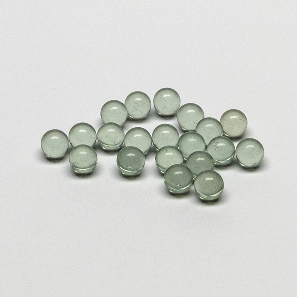 Das Bild zeigt eine Ansammlung von kleinen, transparenten Glaskugeln in verschiedenen Grüntönen. Sie sind gleichmäßig geformt und auf einer hellen Oberfläche angeordnet, was darauf hinweist, dass sie als Experimentiermaterial verwendet werden könnten.