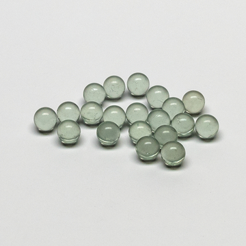 Das Bild zeigt eine Ansammlung von kleinen, transparenten Glaskugeln in verschiedenen Grüntönen. Sie sind gleichmäßig geformt und auf einer hellen Oberfläche angeordnet, was darauf hinweist, dass sie als Experimentiermaterial verwendet werden könnten.