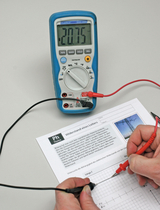 Auf dem Bild ist ein digitales Multimeter zu sehen, das einen Widerstand von 2,075 kΩ anzeigt. Daneben steht ein Arbeitsblatt mit dem Titel „Widerstand eines Leiters“, während eine Person mit zwei Messleitungen eine Verbindung zum Leiter herstellt und Notizen macht.
