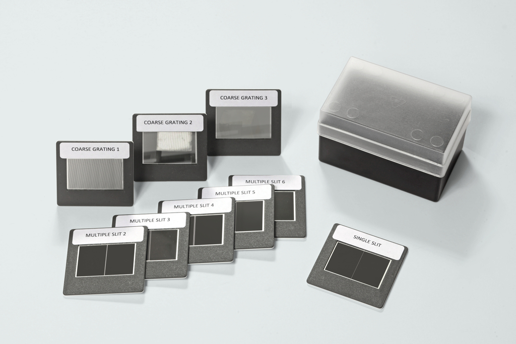 Das Bild zeigt eine Sammlung von optischen Gitter- und Spaltmustern, die für Experimente in der Physik genutzt werden. Die Muster sind in einer praktischen Aufbewahrungsbox angeordnet und beschriftet, um die Identifikation zu erleichtern.