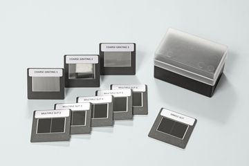 Das Bild zeigt eine Sammlung von optischen Gitter- und Spaltmustern, die für Experimente in der Physik genutzt werden. Die Muster sind in einer praktischen Aufbewahrungsbox angeordnet und beschriftet, um die Identifikation zu erleichtern.