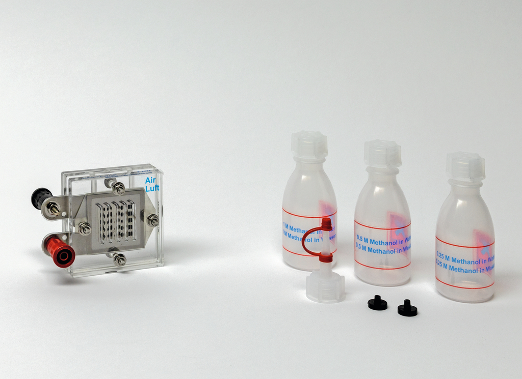 Das Bild zeigt ein transparentes Messgerät mit Anschlüssen für Luft sowie drei Flaschen, die Methanol-Lösungen in unterschiedlichen Konzentrationen enthalten. Zusätzlich sind zwei schwarze Verschlüsse und ein Verbindungsstück abgebildet.