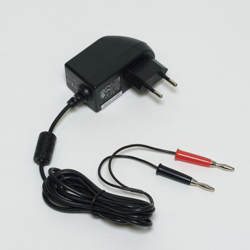 Das Bild zeigt ein schwarzes Netzteil mit einem Eurostecker und zwei Kabeln mit Krokodilklemmen in Rot und Schwarz. Es ist für den Einsatz in Experimenten im Bildungswesen konzipiert und stellt eine Verbindung für elektrische Anwendungen her.