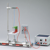 Das Bild zeigt ein Experimentiergerät, das aus einem Rahmen mit elektrischem Anschluss und einem schwebenden, farblich markierten Block besteht. Es dient zur Untersuchung von physikalischen Phänomenen wie Magnetismus oder elektromagnetischen Feldern im Bildungsbereich.
