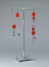 Das Bild zeigt eine experimentelle Vorrichtung mit einem Ständer und mehreren roten Rollen, an denen Gewichte unterschiedlich platziert sind. Diese Apparatur dient zur Durchführung von physikalischen Experimenten, beispielsweise zur Demonstration von Kräften und Bewegungen.