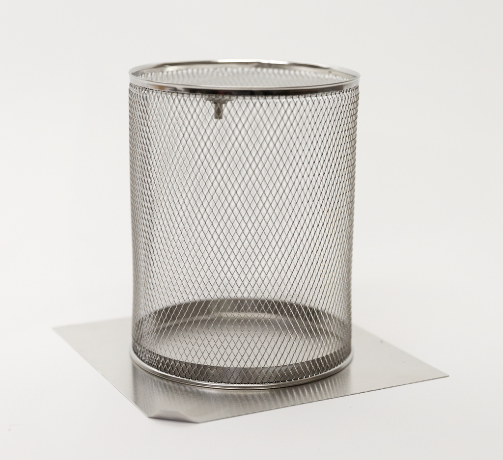 Das Bild zeigt einen runden, metallenen Drahtbehälter mit einem stabilen Boden, der auf einer rechteckigen Metallplatte steht. Dieser Behälter könnte für Experimente in Bildungseinrichtungen verwendet werden, um Materialien zu halten oder zu filtern.