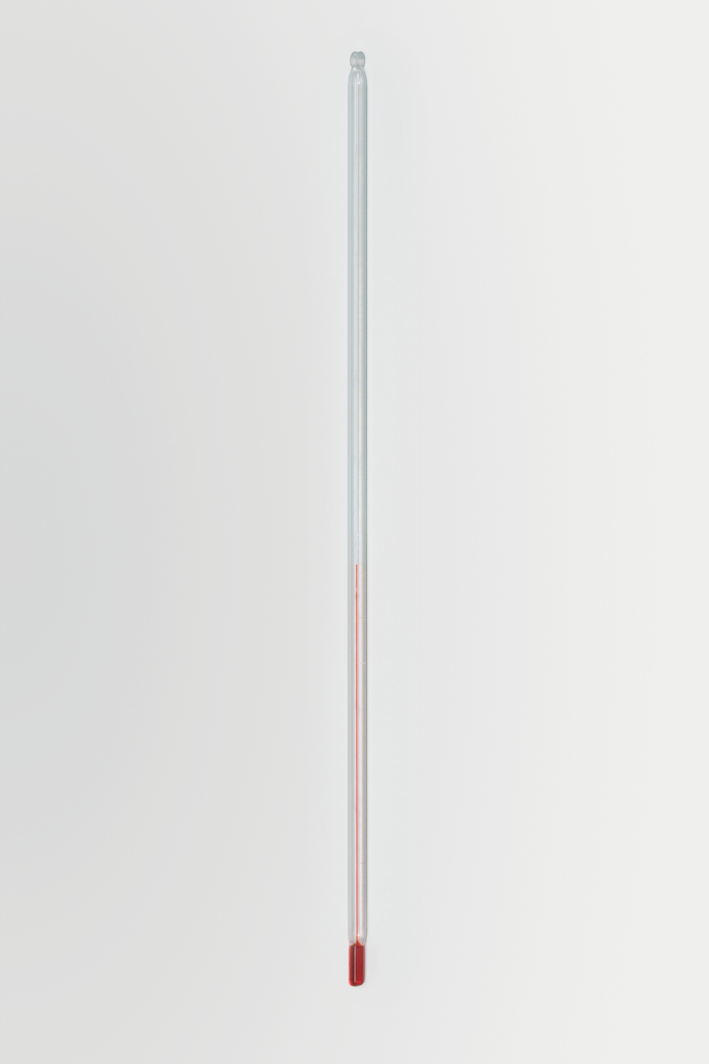 Das Bild zeigt ein transparentes Glasthermometer mit einer roten Flüssigkeit, die den Temperaturstand anzeigt. Es ist auf einem weißen Hintergrund platziert und eignet sich für Experimente im Bildungsbereich.