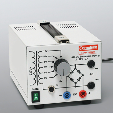 Das Bild zeigt eine AC-DC-Stromversorgungseinheit, die von der Marke Cornelsen Experiminta gefertigt wurde. Sie ist mit verschiedenen Spannungsoptionen von 2V bis 12V und einem Drehregler zur Einstellung der Ausgangsspannung ausgestattet.