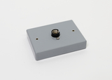 Das Bild zeigt ein graues Gehäuse mit einer Federkontaktbuchse in der Mitte. Es verfügt zudem über zwei kleine Löcher, die vermutlich zur Befestigung dienen.