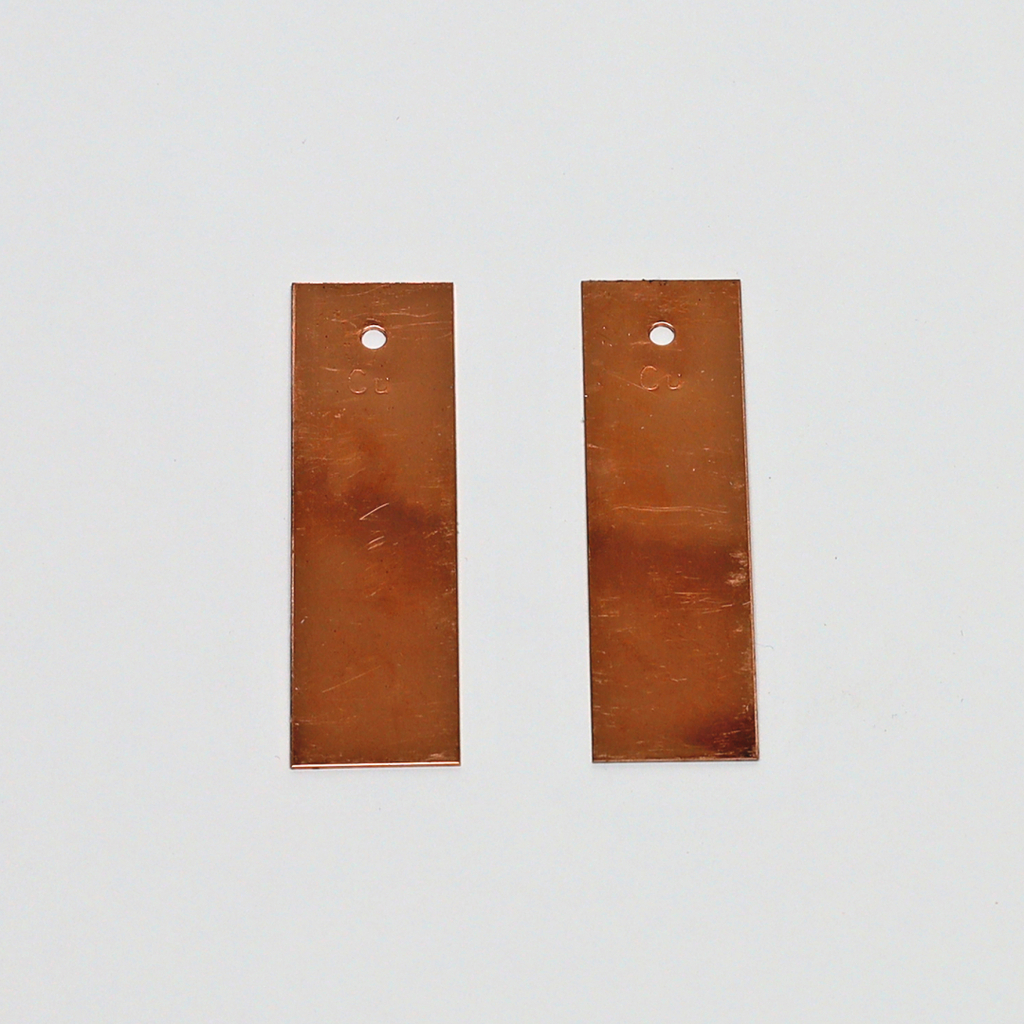 Das Bild zeigt zwei rechteckige Kupferplatten mit einem Loch an der oberen Kante. Diese Platten sind typischerweise für Experimente in der Elektrizitätslehre oder Chemie im Bildungsbereich geeignet.