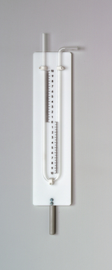 Das Bild zeigt ein Experimentiergerät, das zur Messung von Druck verwendet wird. Es besteht aus einer horizontalen Röhre mit einer Skala von 0 bis 10 und einem Metallgriff für die Bedienung.