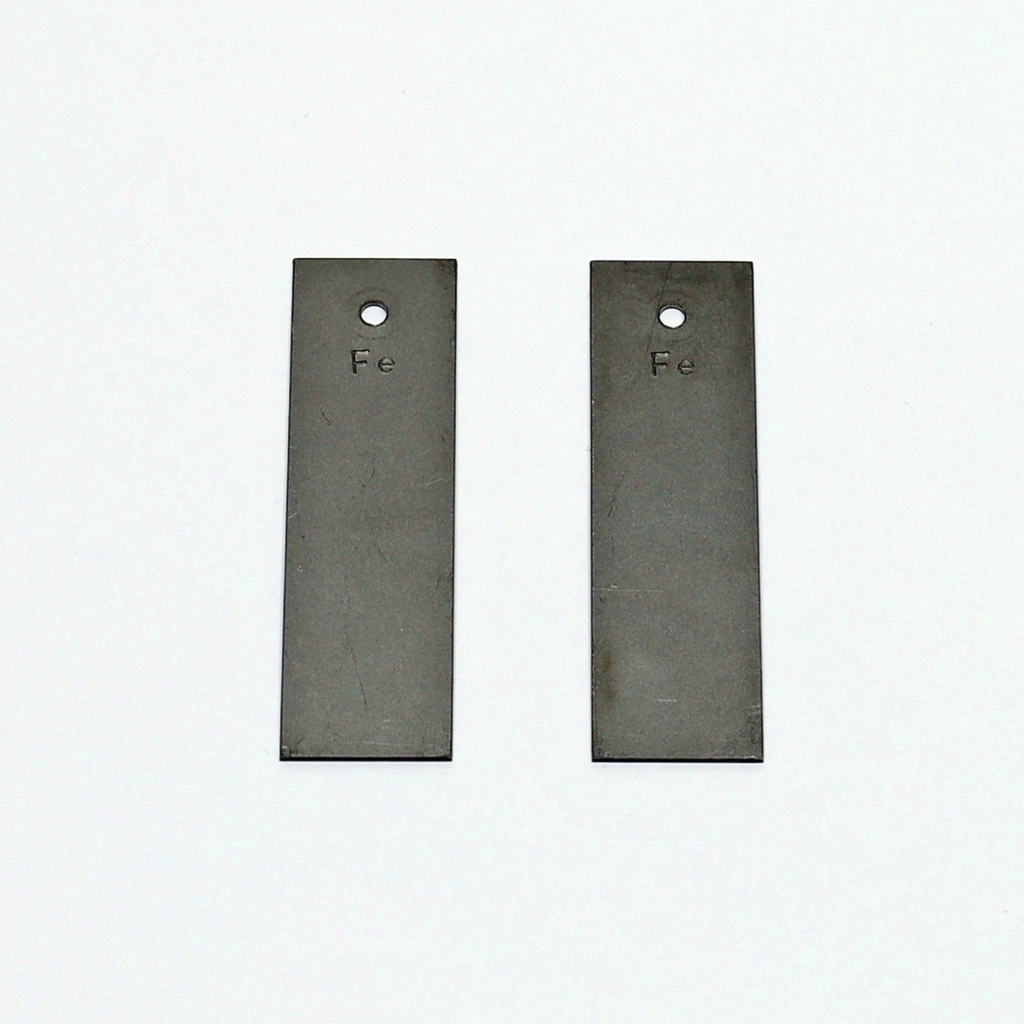 Das Bild zeigt zwei rechteckige Metallplatten, die aus Eisen (Fe) bestehen. Jede Platte ist mit einem Loch versehen, was auf ihre Verwendung in Experimenten oder in der Bildungsarbeit hinweist.