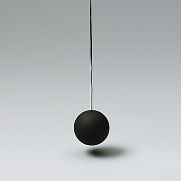 Das Bild zeigt eine schwarze Pendelkugel, die an einem dünnen Draht hängt. Der Hintergrund ist neutral und hebt das Exemplar deutlich hervor, was für Experimente im Bildungswesen geeignet ist.