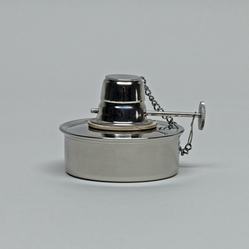 Das Bild zeigt einen Edelstahl-Brenner, der typischerweise in labortechnischen Experimenten verwendet wird. Er besitzt einen mittigen Docht und eine Schutzkappe, die mit einer Kette verbunden ist.