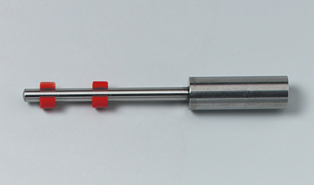 Das Bild zeigt ein Experimentiergerät aus Metall mit einer glatten Oberfläche und zwei roten Kunststoffringen. Es könnte sich um ein Werkzeug für physikalische Experimente oder Demonstrationen handeln.