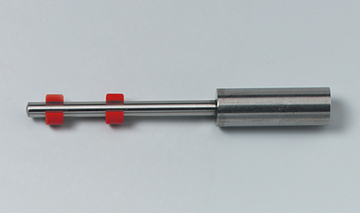 Das Bild zeigt ein Experimentiergerät aus Metall mit einer glatten Oberfläche und zwei roten Kunststoffringen. Es könnte sich um ein Werkzeug für physikalische Experimente oder Demonstrationen handeln.