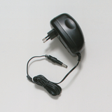 Das Bild zeigt ein schwarzes Netzteil mit einem Eurostecker, das für die Stromversorgung elektrischer Geräte verwendet wird. Es hat ein abgehendes Kabel mit einem Rundstecker für den Anschluss an verschiedene Geräte oder Experimentierbedarf.