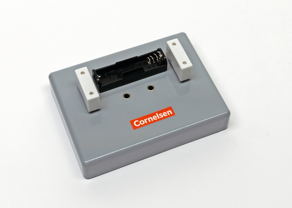 Das Bild zeigt ein graues Experimentiergerät mit einer Batteriefachöffnung und zwei weißen Anschlussleisten. Es ist für den Bildungsbereich konzipiert und trägt das Logo von Cornelsen.