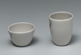 Das Bild zeigt zwei weiße Keramiktassen: eine kleinere, rundliche Schale und eine höhere, zylindrische Tasse. Beide Tassen scheinen für experimentelle Zwecke im Bildungsbereich geeignet zu sein, möglicherweise für chemische Versuche.