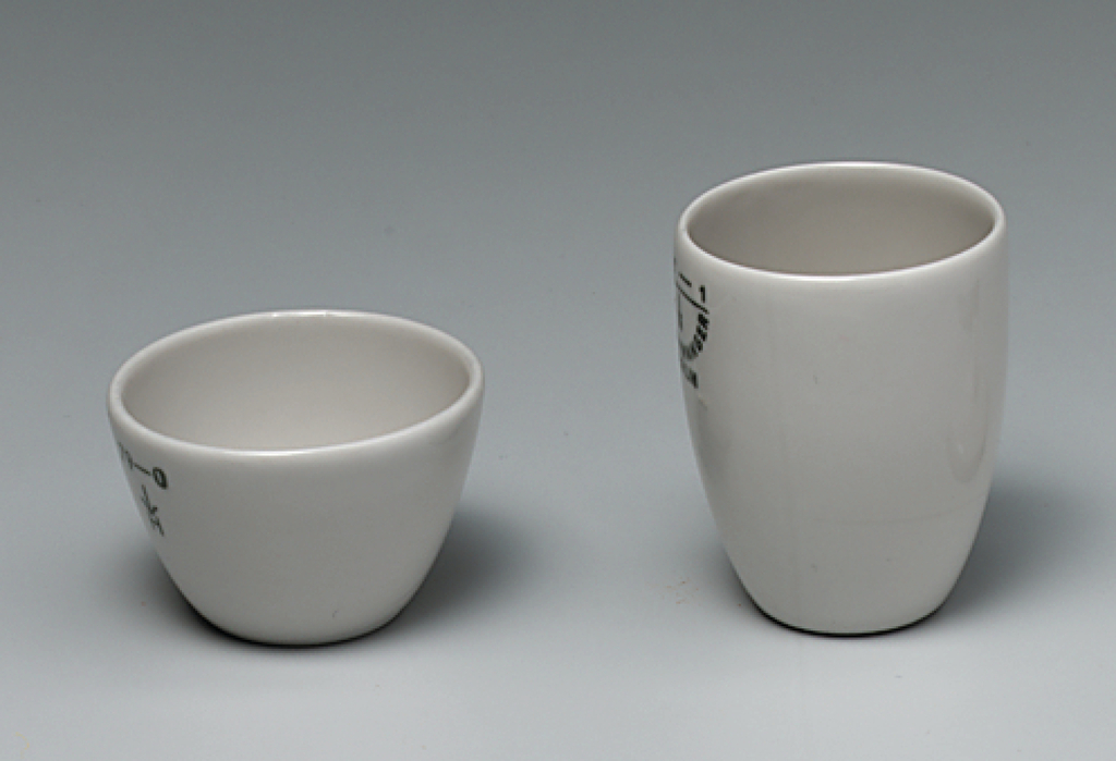 Das Bild zeigt zwei weiße Keramiktassen: eine kleinere, rundliche Schale und eine höhere, zylindrische Tasse. Beide Tassen scheinen für experimentelle Zwecke im Bildungsbereich geeignet zu sein, möglicherweise für chemische Versuche.
