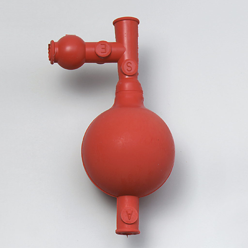 Das Bild zeigt ein rotes Gummigerät mit einer kugelförmigen Basis und mehreren Anschlüssen. Es wird wahrscheinlich als Teil von Experimentierbedarf im Bildungsbereich verwendet, um verschiedene chemische oder physikalische Prozesse zu demonstrieren.