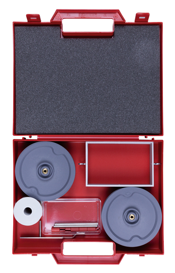 Das Bild zeigt einen roten Kunststoffkoffer, der geöffnet ist und verschiedene Experimentiermaterialien enthält. Darin sind zwei graue Scheiben, ein Behälter, eine Papierrolle und weitere kleine Utensilien, die für Experimentierzwecke verwendet werden können.