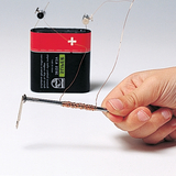 Das Bild zeigt eine Hand, die einen mit Draht umwickelten Nagel hält, der an einer Batterie angeschlossen ist. Dies illustriert ein einfaches Experiment zur Demonstration von Elektromagnetismus im Bildungsbereich.