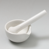 Auf dem Bild sind ein weißes Porzellan-Mörser und ein Stößel zu sehen. Diese Werkzeuge werden häufig im Labor und im Bildungsbereich verwendet, um Materialien zu zerkleinern oder zu mischen.