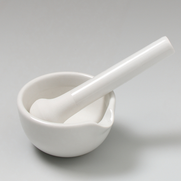 Auf dem Bild sind ein weißes Porzellan-Mörser und ein Stößel zu sehen. Diese Werkzeuge werden häufig im Labor und im Bildungsbereich verwendet, um Materialien zu zerkleinern oder zu mischen.