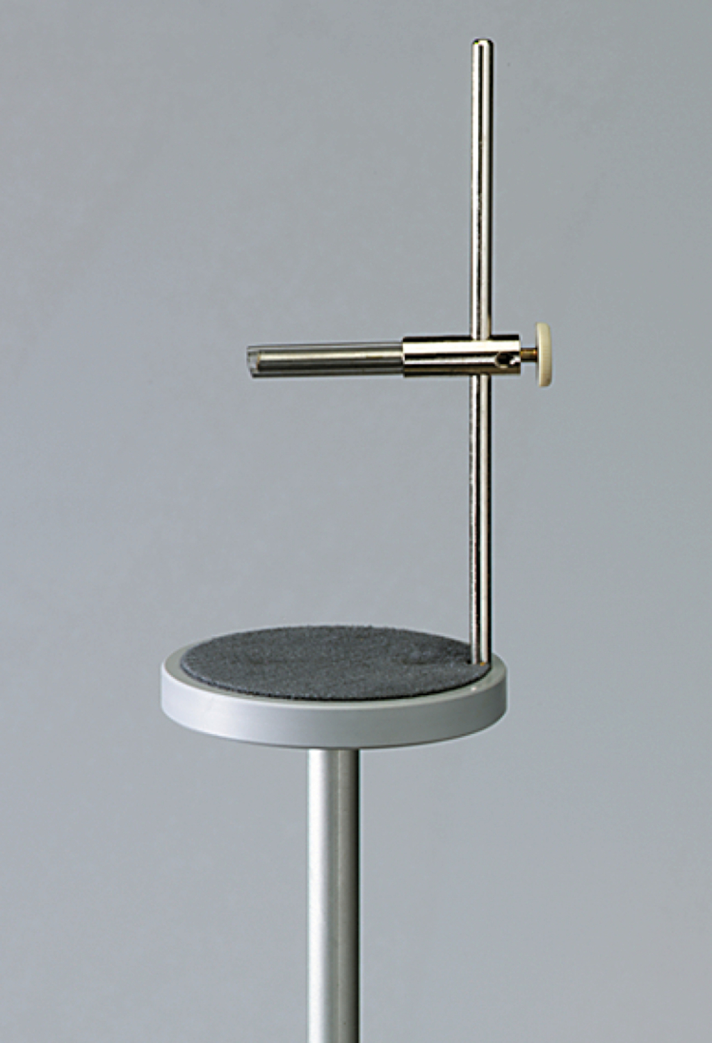 Das Bild zeigt ein Experimentiergerät, das aus einem stabilen Standfuß und einem senkrechten Metallstangen besteht. An einer horizontalen Stange sind verschiedene Halterungen angebracht, die für chemische oder physikalische Experimente genutzt werden können.