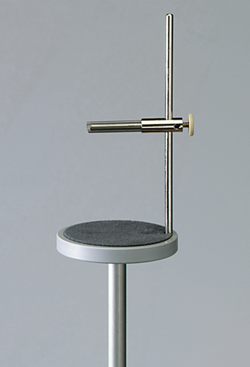 Das Bild zeigt ein Experimentiergerät, das aus einem stabilen Standfuß und einem senkrechten Metallstangen besteht. An einer horizontalen Stange sind verschiedene Halterungen angebracht, die für chemische oder physikalische Experimente genutzt werden können.