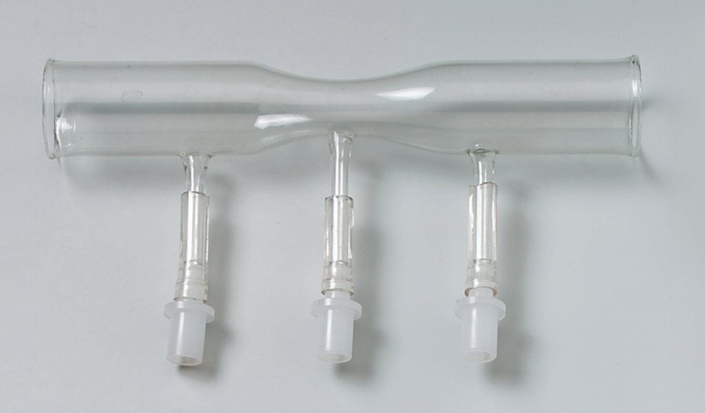 Das Bild zeigt ein Glasgerät mit drei Rohren, das vermutlich für chemische Experimente verwendet wird. Es hat zwei seitliche Auslässe und einen zentralen Verbindungspunkt, was auf eine Funktion zur Gas- oder Flüssigkeitsübertragung hinweist.