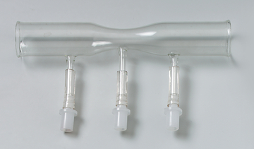 Das Bild zeigt ein Glasgerät mit drei Rohren, das vermutlich für chemische Experimente verwendet wird. Es hat zwei seitliche Auslässe und einen zentralen Verbindungspunkt, was auf eine Funktion zur Gas- oder Flüssigkeitsübertragung hinweist.