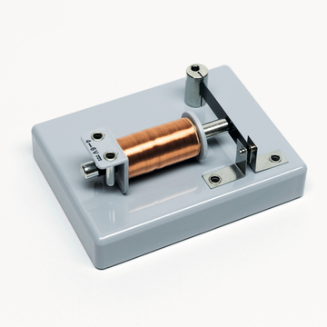 Das Bild zeigt ein Experimentiergerät mit einer Kupferdrahtspule, einem beweglichen Metallstück und einer stabilen Basis. Es dient wahrscheinlich zur Demonstration von physikalischen Prinzipien, wie Magnetismus oder Elektromagnetismus, im Bildungsbereich.
