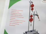 Das Bild zeigt ein physikalisches Experimentiergerät mit mehreren Rollen, einem Haken und einer Federwaage, das zur Veranschaulichung grundlegender mechanischer Prinzipien dient. Neben dem Gerät stehen verschiedene Themen wie Hooke'sches Gesetz und Hebelgesetz aufgelistet.