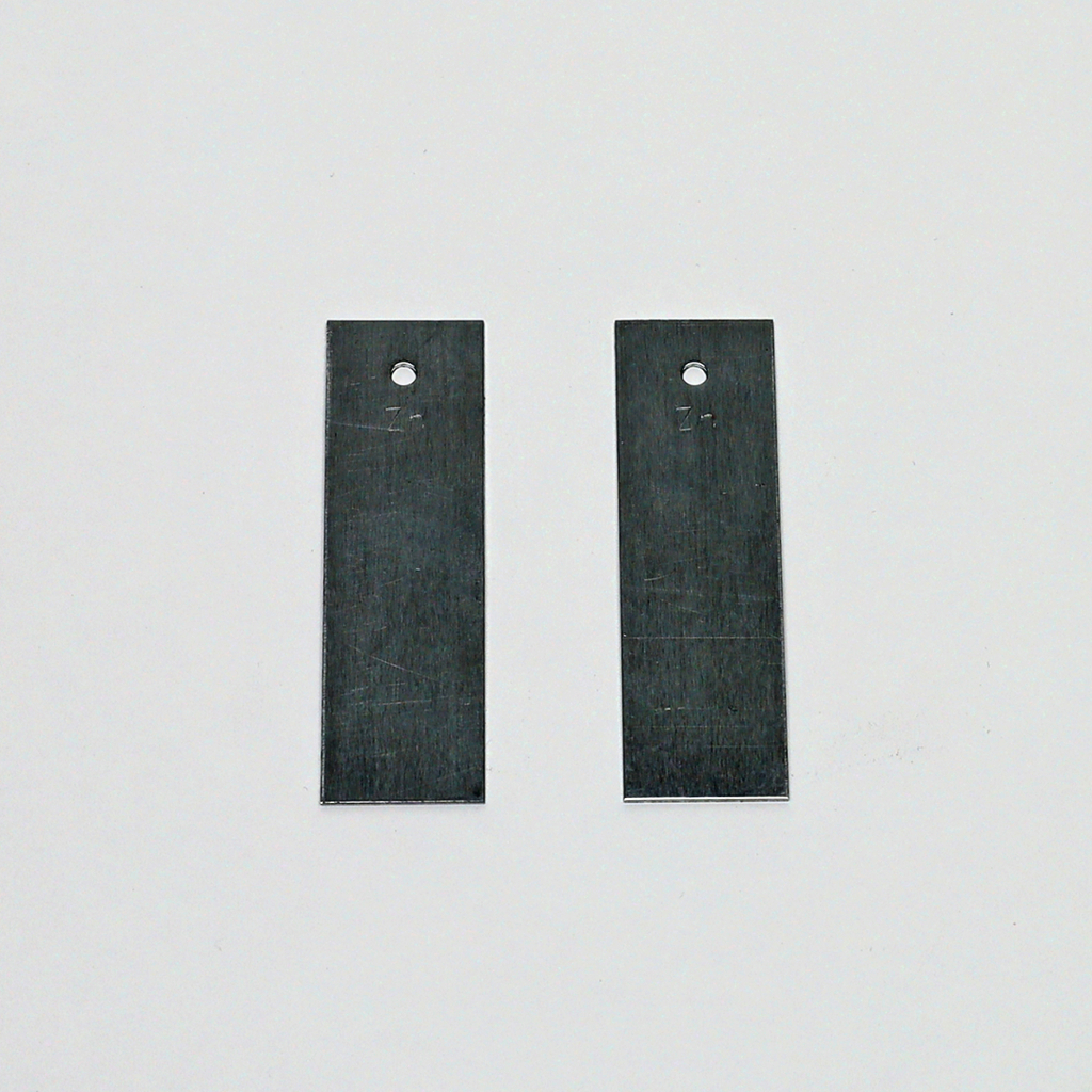 Das Bild zeigt zwei flache Metallstücke mit einer perforierten Stelle. Sie scheinen Teil eines Experimentierbedarfsets zu sein, möglicherweise für den schulischen Einsatz in naturwissenschaftlichen Fächern.