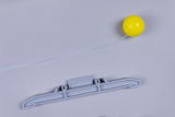 Das Bild zeigt ein graues Bauteil und eine gelbe Kugel, die durch einen Faden miteinander verbunden sind. Diese Komponenten könnten für Experimente im naturwissenschaftlichen Unterricht verwendet werden, um physikalische Prinzipien zu veranschaulichen.