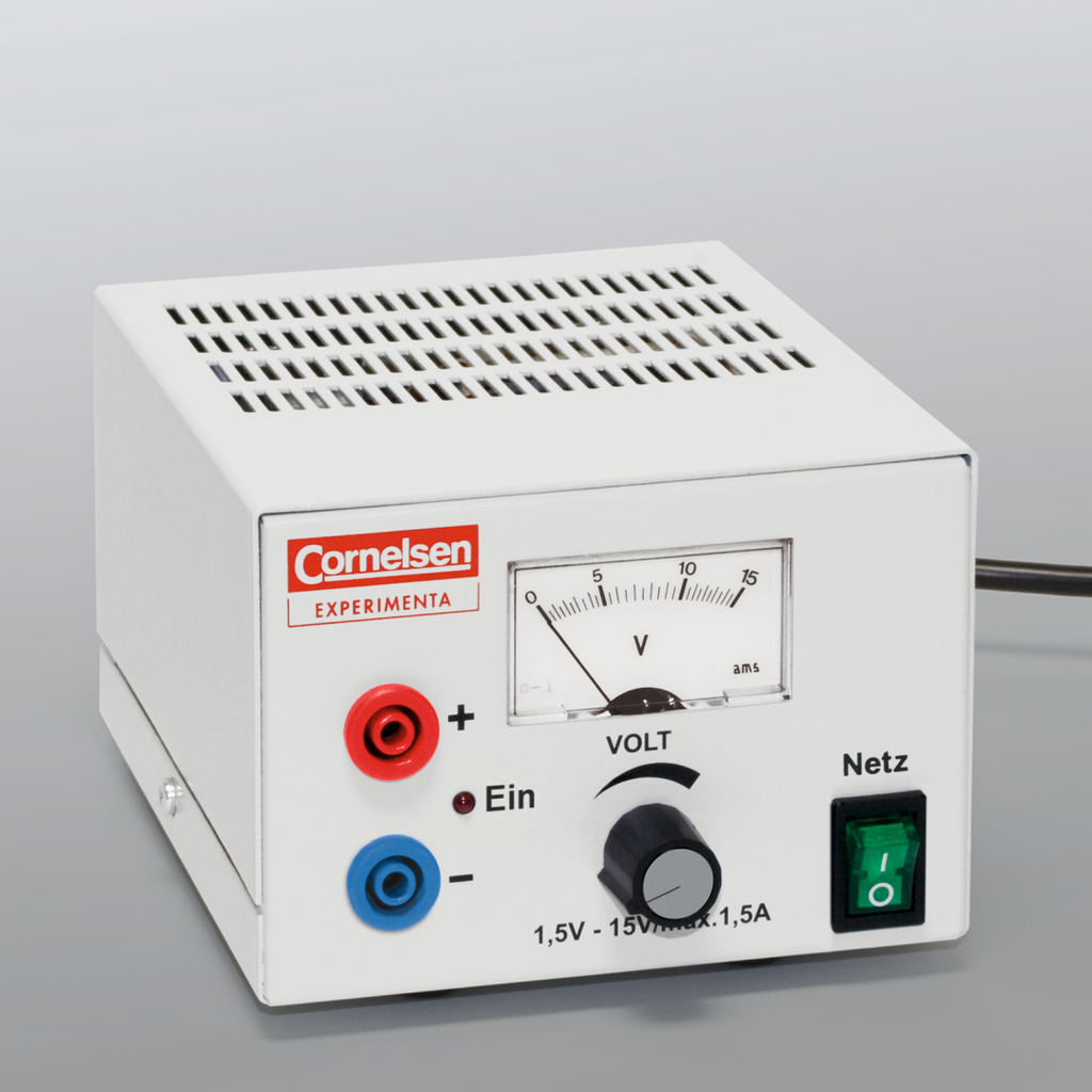 Das Bild zeigt ein elektrisches Experimentiergerät mit einem weißen Gehäuse, das über Anschlüsse für Plus- und Minuspol sowie einen Drehregler zur Spannungsanpassung verfügt. Eine Skala zeigt die Spannung in Volt an, und das Gerät hat einen Netzschalter.