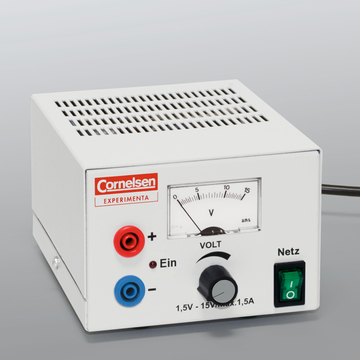 Das Bild zeigt ein elektrisches Experimentiergerät mit einem weißen Gehäuse, das über Anschlüsse für Plus- und Minuspol sowie einen Drehregler zur Spannungsanpassung verfügt. Eine Skala zeigt die Spannung in Volt an, und das Gerät hat einen Netzschalter.