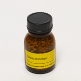 Das Bild zeigt ein braunes Fläschchen mit einer schwarzen Schraubkappe, das mit einem gelben Etikett versehen ist. Das Etikett trägt die Aufschrift „Siedesteinchen“, und die Verpackung enthält kleine, körnige Substanzen, die für chemische Experimente verwendet werden.