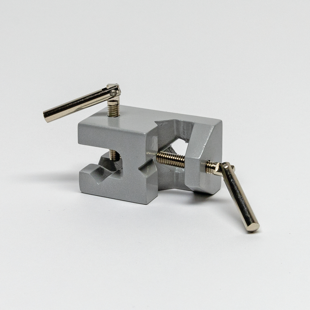 Das Bild zeigt einen grauen Experimentierklemmenhalter, der zur Befestigung von Materialien in wissenschaftlichen Experimenten verwendet wird. Er verfügt über Schrauben, um die Spannung einzustellen, und lässt sich somit leicht an verschiedene Objekte anpassen.