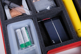 Das Bild zeigt ein Experimentierkit, das verschiedene Komponenten enthält, darunter eine Solarzelle, Batterien, ein Glasröhrchen und andere Materialien, die in einem schaumstoffgepolsterten Behälter angeordnet sind. Diese Ausrüstung eignet sich für Bildungszwecke im Bereich Naturwissenschaften.