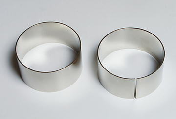 Das Bild zeigt zwei metallene Ringe, die für Experimente verwendet werden können. Der linke Ring ist vollständig, während der rechte Ring eine ausgeschnittene Öffnung hat, was unterschiedliche Einsatzmöglichkeiten bei Experimenten ermöglicht.