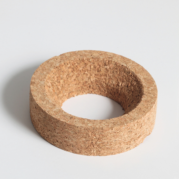 Das Bild zeigt einen ringförmigen Korkblock, der eine rauhe Oberfläche und eine mittige Vertiefung aufweist. Der Kork eignet sich möglicherweise für Experimente im Bildungsbereich, etwa als Halterung oder Unterstützung für verschiedene Materialien.
