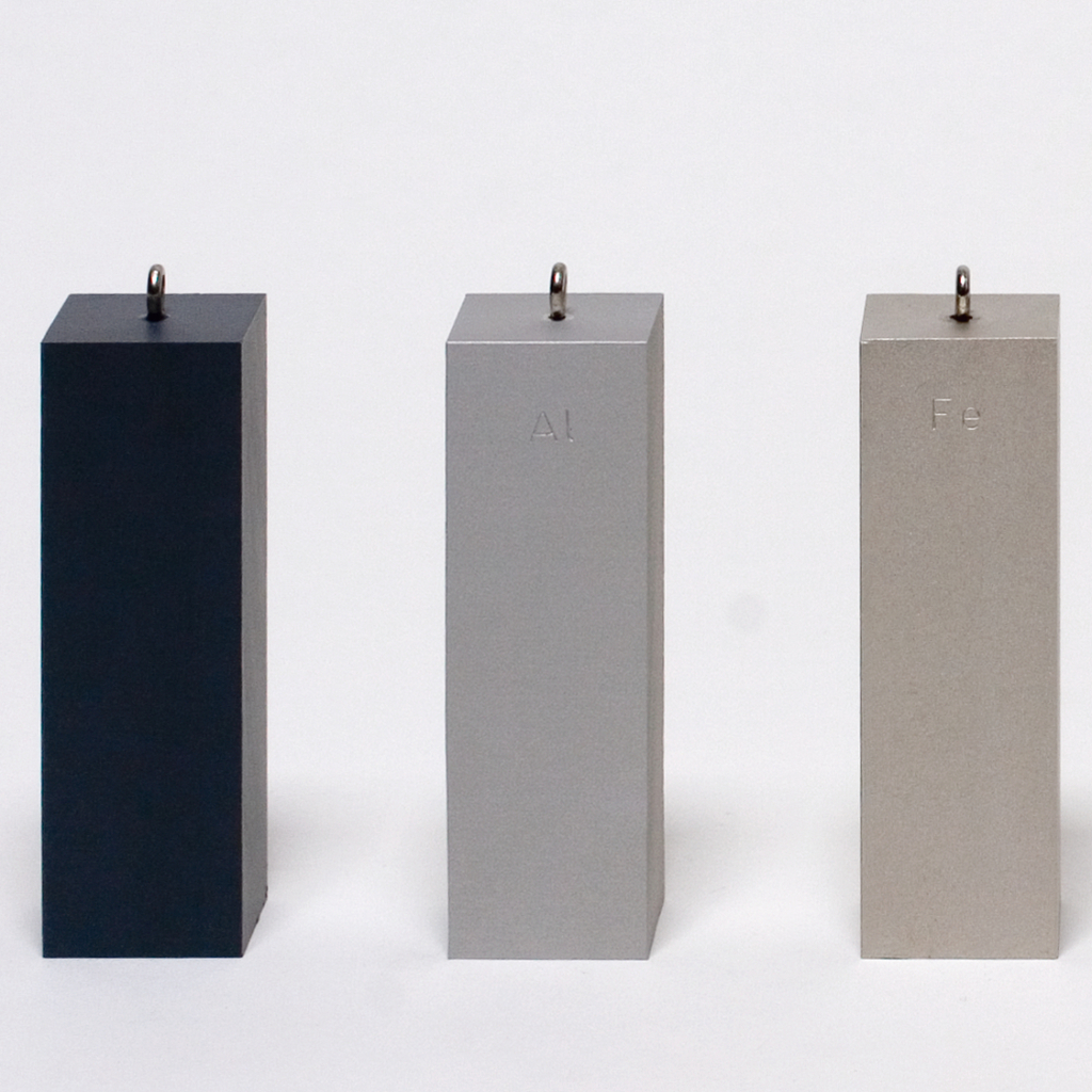 Das Bild zeigt drei rechteckige Blöcke aus unterschiedlichen Materialien, die in einem Experimentierbedarf-Shop angeboten werden. Die Blöcke sind beschriftet mit den chemischen Symbolen für Aluminium (Al) und Eisen (Fe) sowie einem dunklen Block, dessen Material nicht identifiziert ist.