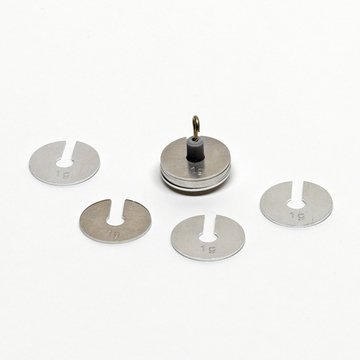 Das Bild zeigt eine Gruppe von Metallgewichten, die zum Experimentieren im Bildungsbereich verwendet werden können. Im Zentrum steht ein Gewicht mit einem Aufhängering, umgeben von weiteren Gewichten, die jeweils mit "1 g" beschriftet sind.